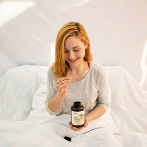 Eine Frau sitzt im Bett und hält Bionutra Bio Ashwagandha Kapseln in der Hand